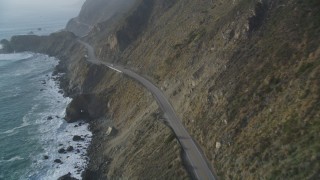 DFKSF03_112 - 5K aerial stock footage of following Highway 1 coastal road past cliffs, tracking a white car, Big Sur, California