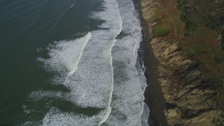 DFKSF15_047 - 5K aerial stock footage of a reverse view of ocean waves rolling toward a beach and coastal cliffs, Lakeshore District, San Francisco, California