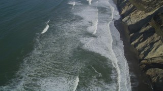 DFKSF15_049 - 5K aerial stock footage of a reverse view of ocean waves rolling into coastal cliffs, Daly City, California