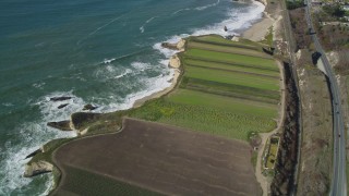 DFKSF15_114 - 5K aerial stock footage of a reverse view of crop fields by Highway 1, train tracks, Davenport, California