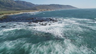 DFKSF16_095 - 5K stock footage aerial video tilt from ocean, reveal seagulls flying over rocks along coast, Big Sur, California