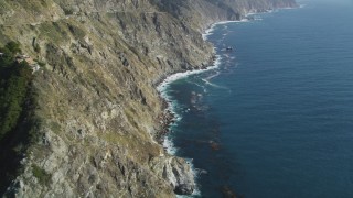 DFKSF16_113 - 5K stock footage aerial video of flying over rocky beach, tilting up along coastal cliffs, Big Sur, California