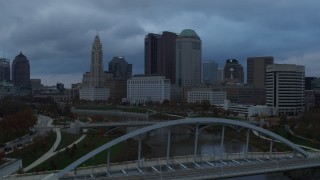 DX0001_002745 - 5.7K aerial stock footage of the city skyline seen from bridge spanning the Scioto River at sunset, Downtown Columbus, Ohio