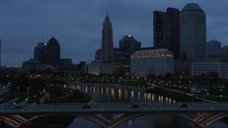 DX0001_002766 - 5.7K aerial stock footage descend by the river to reveal bridge, with view of city skyline at twilight in Downtown Columbus, Ohio