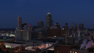DX0001_002973 - 5.7K aerial stock footage of giant skyscrapers of the city skyline at twilight, seen from factory smoke stacks, Downtown Indianapolis, Indiana