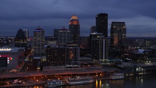 DX0001_003098 - 5.7K aerial stock footage of flying by the skyline lit up at twilight, seen during ascent from Ohio River, Downtown Louisville, Kentucky