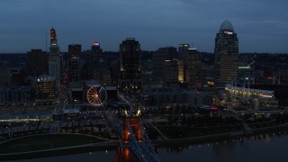 DX0001_003165 - 5.7K aerial stock footage of the city skyline and bridge lit for twilight, and approach from Ohio River, Downtown Cincinnati, Ohio