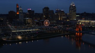 DX0001_003179 - 5.7K aerial stock footage flying by lights of city skyline and bridge at twilight, seen from across river, Downtown Cincinnati, Ohio