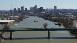 DX0002_112_026 - 5.7K aerial stock footage a barge on the river, sailing toward the city's skyline, seen seen while flying by bridge, Downtown Nashville, Tennessee