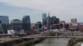 DX0002_116_024 - 5.7K aerial stock footage of slowly passing a river and bridge, focus on skyscrapers in Downtown Nashville, Tennessee