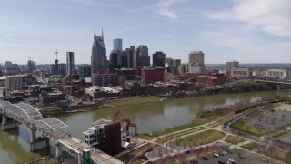 DX0002_117_004 - 5.7K aerial stock footage reverse view of the city's riverfront skyscrapers, descend near pedestrian bridge, Downtown Nashville, Tennessee