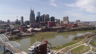 DX0002_117_009 - 5.7K aerial stock footage orbiting city's riverfront skyscrapers across the Cumberland River, seen from pedestrian bridge, Downtown Nashville, Tennessee