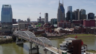 DX0002_117_033 - 5.7K aerial stock footage descend near pedestrian bridge with view of Broadway across the Cumberland River, Downtown Nashville, Tennessee