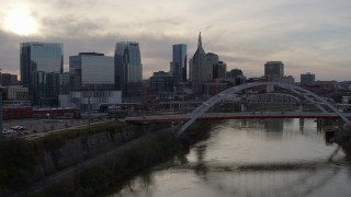 DX0002_119_031 - 5.7K aerial stock footage flyby bridge and river while focused on city skyline at sunset, Downtown Nashville, Tennessee