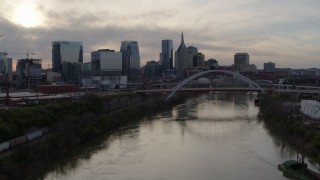 DX0002_119_033 - 5.7K aerial stock footage descend with view of bridge over river and city skyline at sunset, Downtown Nashville, Tennessee