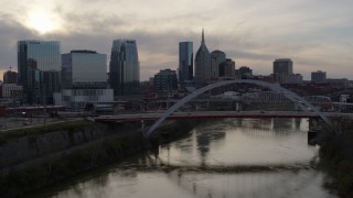 DX0002_119_035 - 5.7K aerial stock footage follow the river to approach the bridge and city skyline at sunset, Downtown Nashville, Tennessee