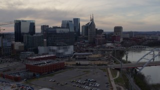 DX0002_119_037 - 5.7K aerial stock footage of flying away from city skyscrapers beside the river at sunset, Downtown Nashville, Tennessee