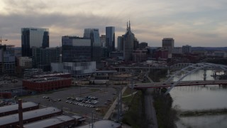 DX0002_119_040 - 5.7K aerial stock footage ascend past bridges and Cumberland River at sunset for view of skyscrapers, Downtown Nashville, Tennessee