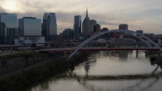 DX0002_119_044 - 5.7K aerial stock footage fly close to bridge on Cumberland River at sunset, skyline in background, Downtown Nashville, Tennessee