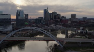 DX0002_119_045 - 5.7K aerial stock footage ascend past bridge on Cumberland River at sunset, skyline in background, Downtown Nashville, Tennessee
