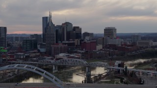 DX0002_120_006 - 5.7K aerial stock footage flying by and away from riverfront skyline, bridges, and Cumberland River at sunset, Downtown Nashville, Tennessee
