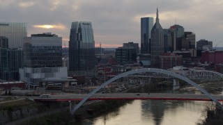 DX0002_120_012 - 5.7K aerial stock footage of the riverfront skyline, ascend past bridge spanning the river at sunset, Downtown Nashville, Tennessee