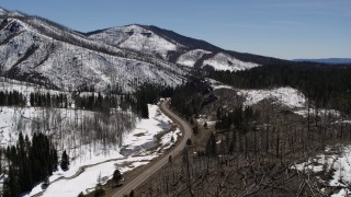 DX0002_134_030 - 5.7K aerial stock footage of following a winding road between snowy mountains and evergreens, New Mexico