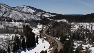 DX0002_134_032 - 5.7K aerial stock footage reverse view of winding road by snowy mountains and trees, New Mexico