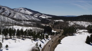 DX0002_134_033 - 5.7K aerial stock footage flyby winding road by snowy mountains, reveal black cars, New Mexico