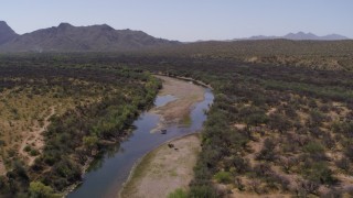 DX0002_141_001 - 5.7K aerial stock footage of following a shallow river through the desert, fly over horses