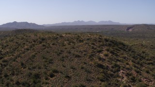 DX0002_141_032 - 5.7K aerial stock footage approach and fly over a hill with green plants and cactus