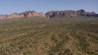 DX0002_141_036 - 5.7K aerial stock footage of passing by desert with green plants and cactus, bordered by mountains