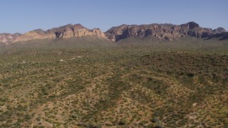 DX0002_141_037 - 5.7K aerial stock footage of a reverse view of desert with green plants and cactus, bordered by mountains