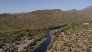 DX0002_141_038 - 5.7K aerial stock footage of passing a narrow river through the desert, then follow it toward a hill
