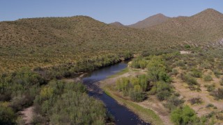 DX0002_141_039 - 5.7K aerial stock footage of following a narrow river bordered by desert hills with cactus