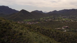 DX0002_145_003 - 5.7K aerial stock footage fly away from homes and golf course, reveal mountain slope with cactus in Tucson, Arizona