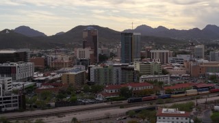 DX0002_145_039 - 5.7K aerial stock footage wide orbit of office towers as a train passes, with Sentinel Peak in the distance, Downtown Tucson, Arizona