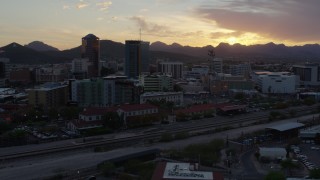 DX0002_146_035 - 5.7K aerial stock footage flying by high-rise office towers and city buildings with view of setting sun in Downtown Tucson, Arizona