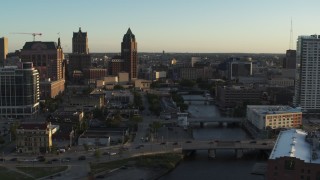 DX0002_150_027 - 5.7K aerial stock footage of city buildings and an office tower by the Milwaukee River at sunset, Downtown Milwaukee, Wisconsin