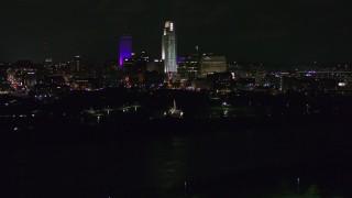 DX0002_173_051 - 5.7K aerial stock footage of a reverse view of tall skyscrapers at night as the fountain lights up, Downtown Omaha, Nebraska