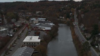 DX0002_220_038 - 5.7K aerial stock footage of flying away from a grocery store by the river at sunset, Montpelier, Vermont