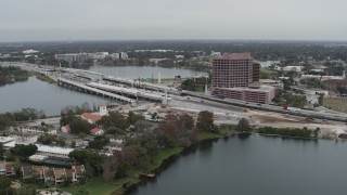 DX0003_233_028 - 5.7K aerial stock footage of flying away from light freeway traffic and office building by a lake in Orlando, Florida