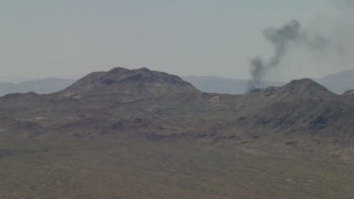 FG0001_000055 - 4K aerial stock footage of a smoke column behind Mojave Desert mountains in San Bernardino County, California