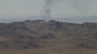 FG0001_000056 - 4K aerial stock footage of a column of black smoke rising behind Mojave Desert mountains in San Bernardino County, California