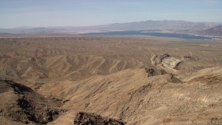 FG0001_000263 - 4K stock footage aerial video pan across desert hills and approach a scarred hill, with Lake Mead in the background, Nevada Desert