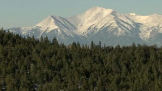 HDA13_322 - HD stock footage aerial video fly over trees-covered ridge to approach snowy Rocky Mountains, Colorado