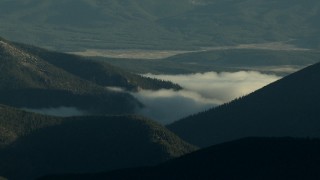 HDA13_438_01 - HD stock footage aerial video of fog and evergreens on mountains, zoom to reveal taller Rocky Mountains at sunrise, Colorado