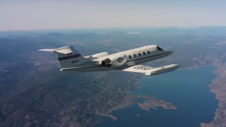 WAAF02_C008_0117ED - 4K stock footage aerial video reveal a Learjet C-21 flying over hills toward a lake in Northern California