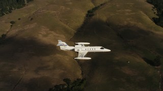 WAAF02_C045_011782 - 4K stock footage aerial video of panning across hills to reveal a Learjet C-21 in flight in Northern California