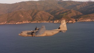 WAAF06_C059_0119W4 - 4K stock footage aerial video of a Lockheed Martin C-130J flying over the ocean at sunset near coast of Northern California